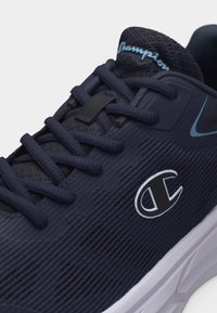 Αθλητικό παπούτσι σε ναυτικό μπλε με μαύρα κορδόνια, υφή στην επάνω επιφάνεια, λευκό λογότυπο Champion στο πλάι και γαλάζιο κείμενο "Champion" στη μαλακή γλώσσα.