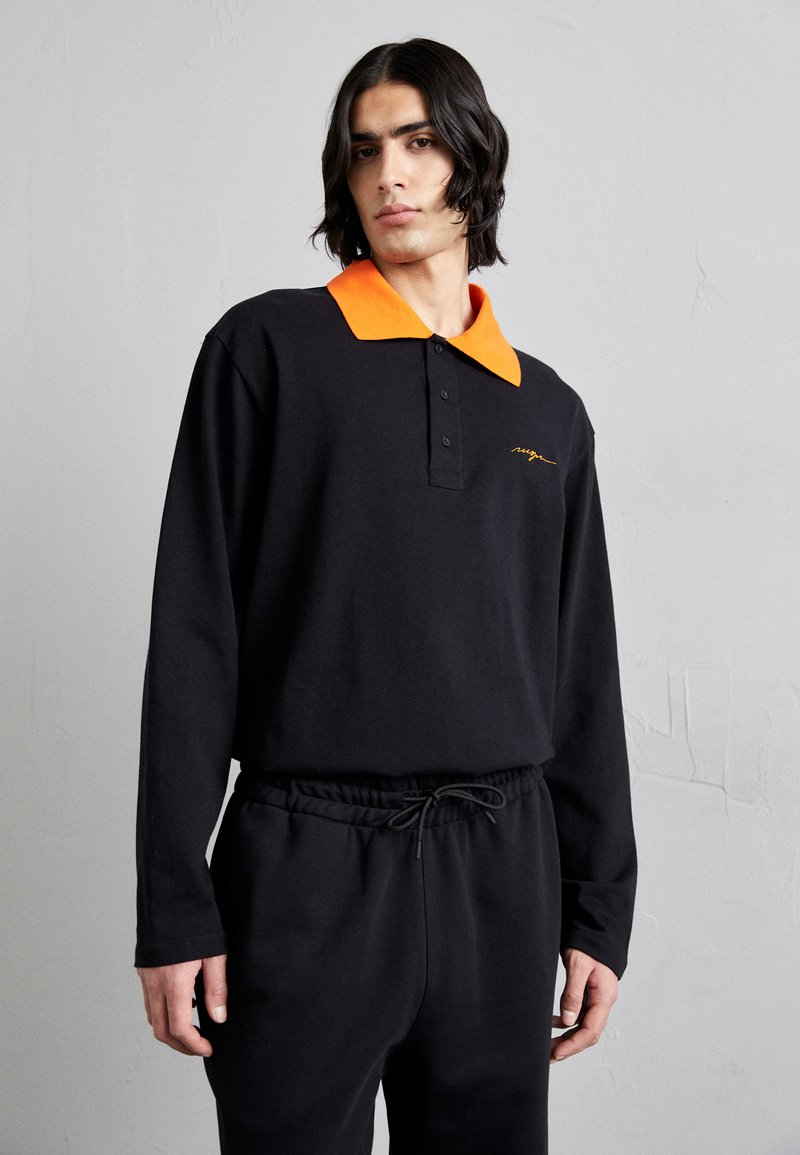 Svart langermet polo med oransje krage, med knappelukking og brodert logo. Kombinert med svarte bukser med snøring.