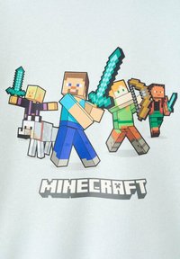 Grafické tričko Minecraft s pixelovanými postavami se meči, psem a lukem na světlém pozadí, pod nimiž je výrazný nápis „MINECRAFT".