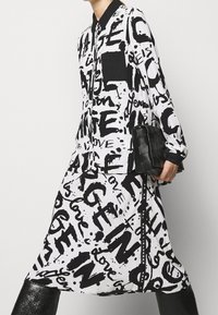 Abito camicia bianco e nero con colletto, caratterizzato da una scritta grafica audace e una tasca nera. Accessoriato con una borsa nera testurizzata.