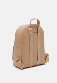 Beżowy plecak o zaokrąglonym kształcie, wykonany z gładkiego materiału sztucznej skóry, z tkaninowymi paskami z logo oraz złotymi akcentami.