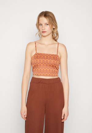 Brun cropped topp med oransje og rød bølgemønster, med tynne stropper. Kombinert med brune, løstsittende, teksturerte høye bukser.