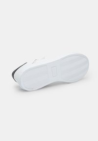 Sneaker bianco con suola in gomma texturizzata, dettagli neri sulla punta e occhielli in metallo per i lacci. La parte inferiore presenta un motivo di battistrada.