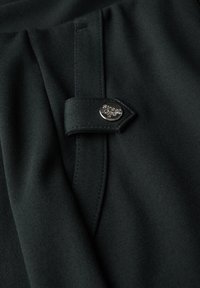 Tissu noir avec une texture lisse, comportant un pli et un bouton argenté gravé "Street One". Couture détaillée visible.