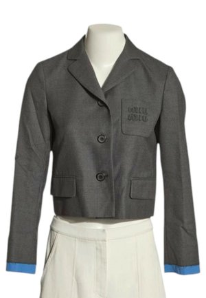 Grå kort blazer med to knapper, blå manchetter, brystlomme med broderi og hvide højtaljede bukser på en mannequin.