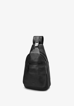 Black leather sling bag with front zipper pocket, adjustable strap, and silver buckle, standing upright on white background.