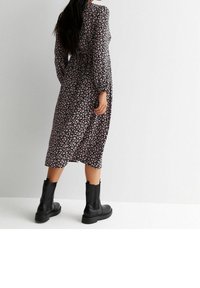 Musta kukkallinen pitkähiha dressi, jossa on solmittava vyötärö ja pieniä vaaleanpunaisia kukkia. Yhdistetty muhkeisiin mustiin nilkkasaappaisiin. Silkkinen kangas.