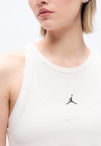 Gros plan d'une personne portant un haut sans manches blanc avec un logo Jumpman noir et un léger swoosh Nike en dessous.