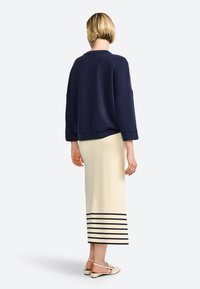 Felpa blu navy con vestibilità ampia e spalle scese, abbinata a una gonna midi color crema con strisce orizzontali blu navy sull'orlo.