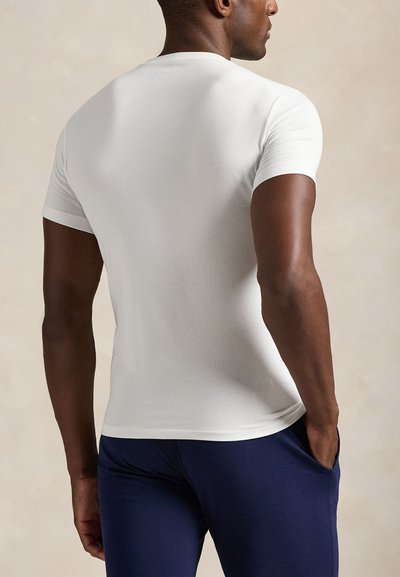 T-shirt moulant à manches courtes blanc en tissu lisse, avec un col rond, associé à un pantalon bleu marine.