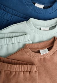 Drie sweatshirts in marineblauw, muntgroen en roestkleur, voorzien van ribbelrokken en een zachte stof. Labels zichtbaar met "NEXT" merk.