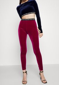 Velvet leggings i fuchsia med ett svart elastiskt midjeband med varumärket. Matchas med en marinblå långärmad crop top och remsandaler.
