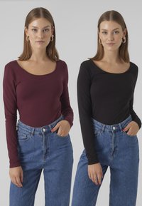 Deux tops à manches longues : un en bordeaux et un en noir, tous deux avec des encolures dégagées. Associés à un jean bleu taille haute. Texture de tissu douce.