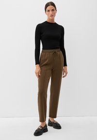 Zwarte geribbelde lange mouwen top gecombineerd met losse, bruine broek met elastische taille. Model draagt zwarte loafers met kettingaccents.