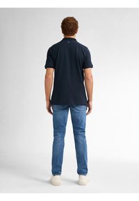 Marineblauwe polo met korte mouwen, van katoen, relaxte pasvorm, gecombineerd met lichtblauwe jeans en witte sneakers. Achteraanzicht weergegeven.