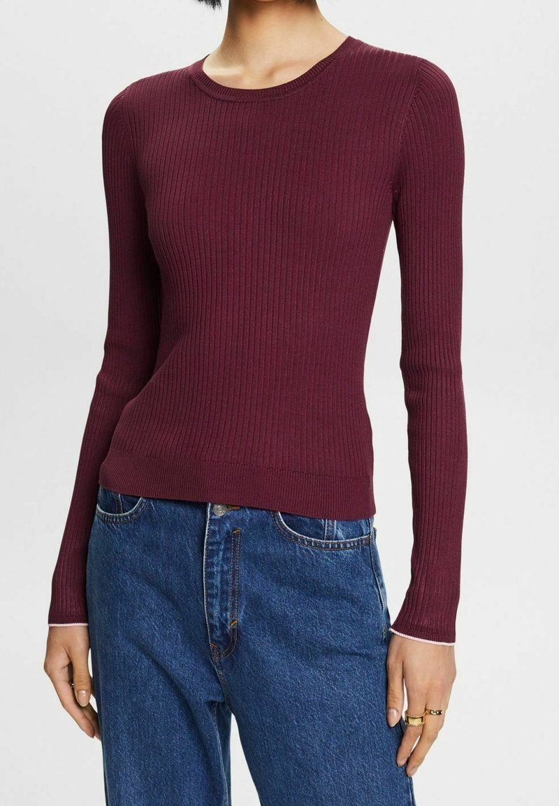 Viininpunainen ribbineulottu pitkähihainen paita pyöreällä kaula-aukkolla, istuva muotoilu ja kontrastiväriset vaaleat reunukset hihojen resoreissa, yhdistetty sinisiin farkkuihin.