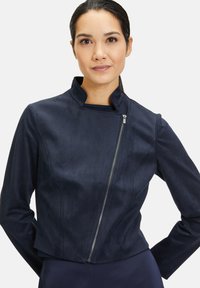 Marinblå faux suede-jacka med hög krage, asymmetrisk dragkedjestängning, långa ärmar och figurnära design, med en mjuk textur.