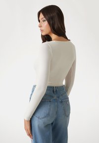 White long-sleeve fitted top paired with light blue high-waisted denim jeans featuring rear pockets and label. Smooth texture, simple design.