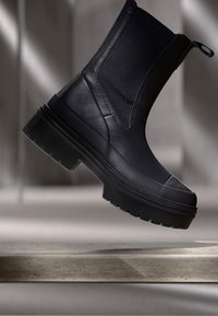 Stivale alla caviglia nero con tomaia in rete testurizzata e accenti in pelle liscia. Suola spessa con battistrada pronunciato. Pannelli laterali elasticizzati per una vestibilità facile.