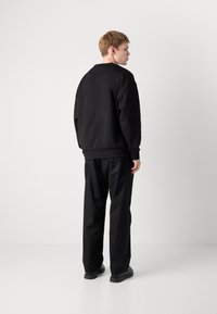 Fekete pulcsi laza szabással, kerek nyakkivágással és bordázott mandzsettákkal, amelyekhez laza fekete nadrágot viselnek. Simas texture, minimalista design.