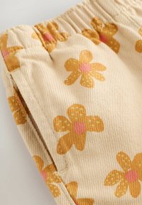 Helles beiges Gewebe mit gerippter Textur, das gelbe und pinke Blumenmuster aufweist. Am oberen Rand ist ein elastischer Bund sichtbar.