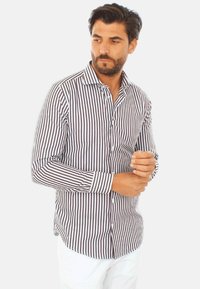 Camicia button-up a righe con sottili righe verticali marroni e bianche, maniche lunghe e colletto classico. Tessuto di cotone leggero.