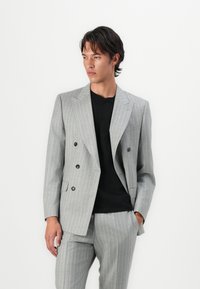 Szürke csíkos blazer, dupla gombolású dizájnnal, fekete gombokkal és slim fit szabással, egyszerű fekete inggel párosítva.
