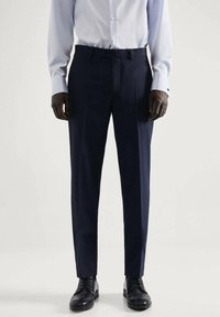 Marineblauwe broek met een getailleerde pasvorm, gemaakt van gelijkmatig materiaal. Heeft een vlakke voorkant, twee zijzakken en een elegante plooi langs de benen.