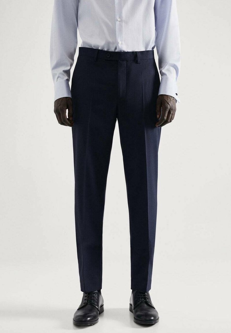 Marineblauwe broek met een getailleerde pasvorm, gemaakt van gelijkmatig materiaal. Heeft een vlakke voorkant, twee zijzakken en een elegante plooi langs de benen.