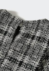 Tissu pied-de-poule texturé noir et blanc avec une petite ouverture fendue au niveau de l'encolure d'un vêtement sur fond blanc.