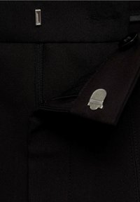 Černé kalhoty vyrobené z texturované látky se zapínáním na zip. Disponují kovovým logem a plochým předním designem s diskrétní kapsou.