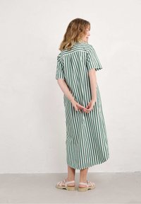 Abito a righe verdi e bianche con maniche corte, lunghezza fino al polpaccio e una vestibilità ampia. Indossato con sandali rosa chiaro, che mostrano un design rilassato.