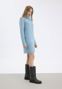 Svetlomodré pletené šaty s vysokým golierom a dlhými rukávmi. V kombinácii s čiernymi čižmami po kolená, ktoré majú strieborné hroty a pracky.