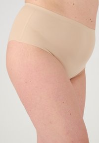 Culotte in cotone beige con una texture liscia e un design a taglio alto, priva di cuciture visibili o embellimenti per un aspetto senza soluzione di continuità.