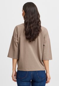 Brun, overdimensioneret T-shirt med trekvartærmer, blød tekstur og rund kant, parret med blå jeans.