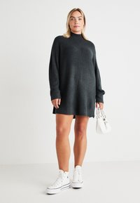 Dark gray ribbed knit dress with a high neck and long sleeves, paired with white high-top sneakers and a small white handbag.