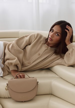 Beige Handtasche mit runder Form, strukturierter Oberfläche, Oberhandgriff und goldenen Hardware-Akzenten. Pullover in passendem Beige mit Knöpfen.