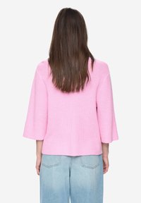 Růžový pletený pulovr volného střihu s tříčtvrtečními rukávy a žebrovanou texturou, v kombinaci se světle modrými džíny s vysokým pasem.