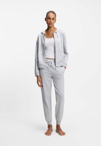 Hellgrauer Kapuzenpullover mit Reißverschluss vorne und Kordelzug, kombiniert mit passenden taillierten Jogginghosen. Weicher Baumwollstoff, elastische Bündchen und Taillenbund.