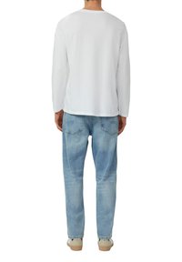 Weißes langärmliges Baumwollhemd, lässige Passform, kombiniert mit hellblauen Jeans. Die Rückansicht zeigt ein schlichtes Design ohne sichtbare Details.