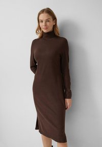 Braun gestricktes Kleid mit hohem Ausschnitt, langen Ärmeln und seitlichem Schlitz, das eine figurbetonte Silhouette und eine weiche Textur bietet.