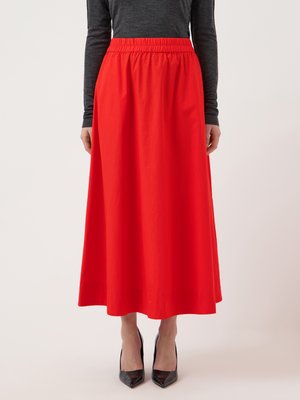 Ženska, oblečena v svetlo rdečo, visokim pasom do gležnjev dolžo krilo z elastičnim pasom, ki ga dopolnjuje temen dolg rokav in črni čevlji s peto.