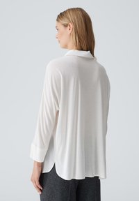 Camicia bianca a maniche lunghe con colletto, caratterizzata da una vestibilità comoda, una texture morbida e un orlo leggermente curvo sul retro.