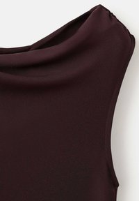 Close-up van donkerbruin stof met een gedrapeerde halslijn en mouwloos ontwerp op een witte achtergrond.