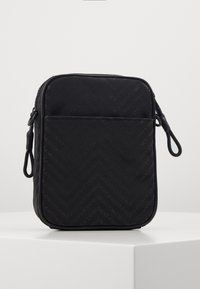 Svart rektangulär väska med ett texturerat mönster av diagonala linjer och varumärkeslogotyp. Har en framficka och dragkedjestängning. Slät tyg.