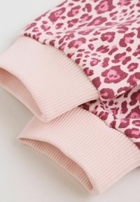 Rosa tygmanschetter med ribbad struktur fästa vid ett rosa och bordeauxfärgat plagg med leopardmönster.