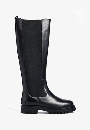 Črne čevlje do kolen s kombinacijo sijajnega usnja in teksturirane tkanine. Debel podplat s grbastim vzorcem in minimalnimi šivi.