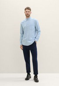 Light blue button-up shirt with a pocket, paired with dark pants and black lace-up shoes. Smooth texture, casual fit.
