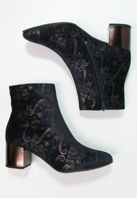 Botas de tobillo de ante negro con un patrón floral en bronce, punta afilada y una cremallera decorativa con un tacón metálico cuadrado.