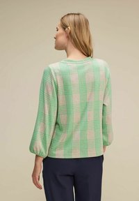 Zielona i beżowa kraciasta bluzka, z długimi rękawami, okrągłym dekoltem i luźnym krojem. Gładka tekstura z wzorzystym wzorem.